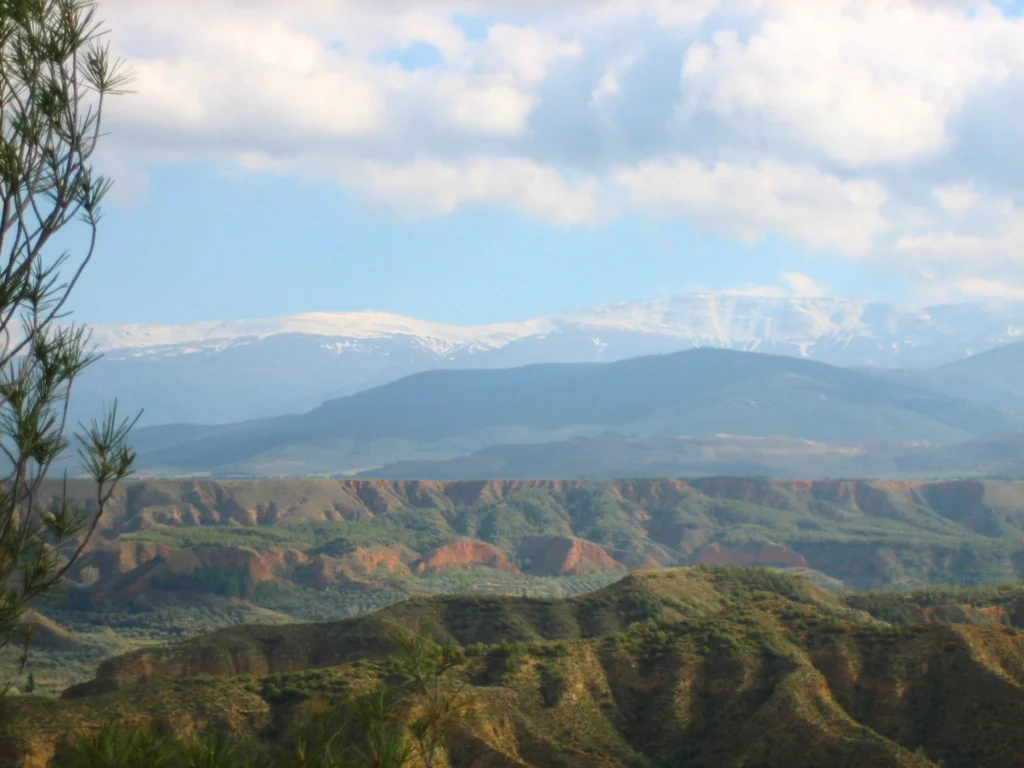 Panorámica de los badlands del Geoparque de Granada con Sierra Nevada al fondo, paisaje natural rodeado de rutas de senderismo cerca de Casa Cueva Alhama en Graena.